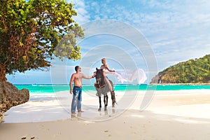 Young couple in love walking with the horse on a tropical beach.