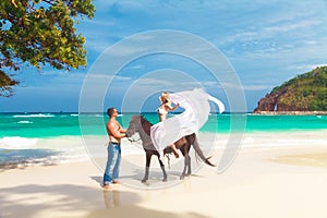 Young couple in love walking with the horse on a tropical beach.