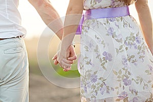 Young couple in love walking in the park holding hands looking in the sunset