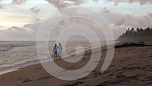 Young couple in love walks on the beach at sunset, holding hands