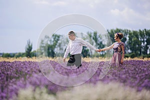 Young couple in love walks holding hands in a lavender field on summer day. girl in a luxurious purple dress