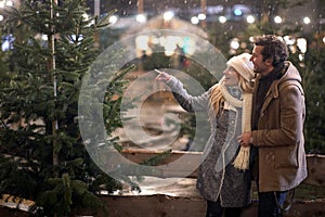 A young couple in love watching a christmas tree on a snowy night in the city. Christmas tree, love, relationship, Xmas, snow