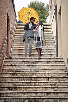 A young couple in love which is descending the stairs in the city during a rainy day. Walk, rain, city, relationship