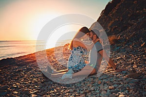 A young couple of lovers embrace sitting on the beach, and pose against the background of the sea and sunset. Side view. The