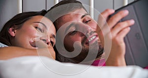 Young Couple Lying In Bed Using Digital Tablet
