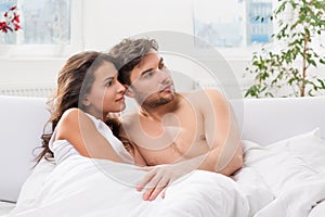 Young couple lying in bed watching television