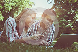 Young couple lying on the grass. Happy couple using laptop.