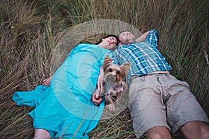 Young couple lying on the grass holding hands and small dog between them