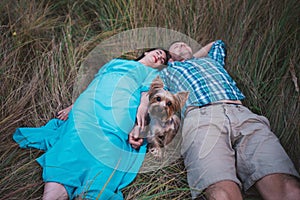 Young couple lying on the grass holding hands and small dog between them