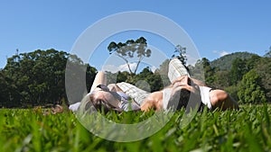 Young couple lying on green grass in park and relaxing. Man and woman sitting on meadow at nature and kissing. Girl and