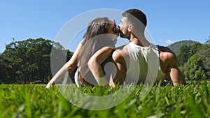 Young couple lying on green grass in park and relaxing. Man and woman sitting on meadow at nature and kissing. Girl and