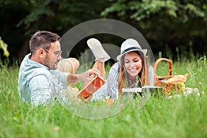 Young couple lying on a picnic blanket, reading books and relaxing