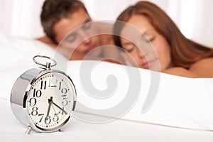 Young couple lying in white bed with alarm clock