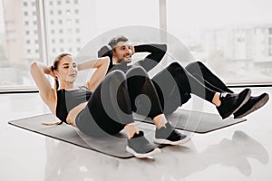 Young couple make sits up at gym. Attractive woman and handsome muscular man are training in light modern gym. Abs exercises