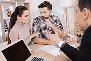 Young couple makes decisions regarding purchase of house sitting in office of real estate agency.