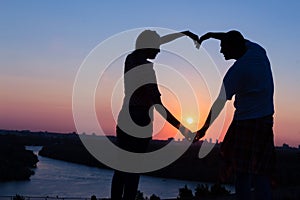 Young couple making heart shape with their hands at sunset