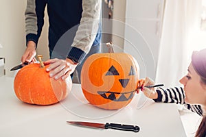 Young couple making jack-o-lantern for halloween on kitchen. Drawing and cutting pumpkin