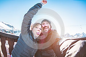 Young couple making selfie in snow resort with background mountains - Tourist laughing and making funny faces on smartphone camera