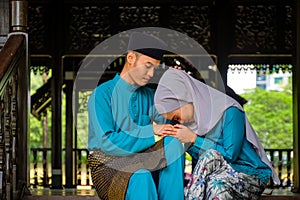 Young couple of malay muslim in traditional costume showing apologize gesture during Aidilfitri celebration at traditional wooden