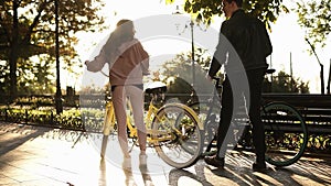 Young couple - man in black casual clothes and woman in pink going to ride their bikes in the summer city park. Rare