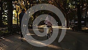 Young couple - man in black casual clothes and woman in pink going to ride their bikes in the summer city park, starting