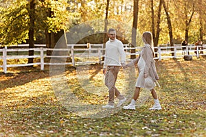 Young couple, man and pregnant wife are holding hands and walking in the autumn park on sunset. Happy family