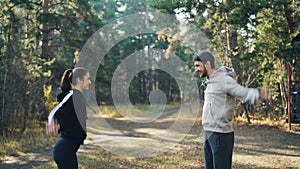 Young couple man and woman are doing sports outdoors in park twirling arms and smiling enjoying warm-up and good company