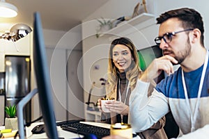 Young couple man and woman drinking coffee and working on PC computer together while sitting at table at home