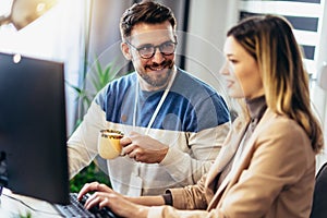 Young couple man and woman drinking coffee and working on PC computer together while sitting at table at home