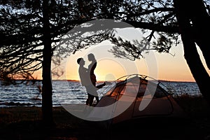 Young couple man and woman having rest at tourist tent and burning campfire on sea shore near forest