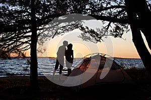 Young couple man and woman having rest at tourist tent and burning campfire on sea shore near forest