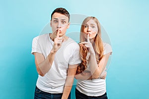 Young couple, man and woman, holding fingers on the lips of the mouth, Hush, secret, showing shhs, on a blue background