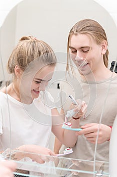 A young couple man and woman with long hair in the morning in front of a bathroom mirror squeeze toothpaste themselves
