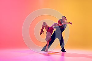 Young couple, man and woman in motion, ballroom dancers making creative performance against gradient pink yellow