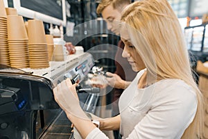 Young couple man and woman owners small business coffee shop, working near coffee machines, making drinks