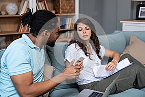 Young couple man and woman, roommates sitting at home on sofa having issue with financial debt, overspending and earnings, cant