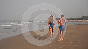 Young couple man and woman run along the sea sandy beach