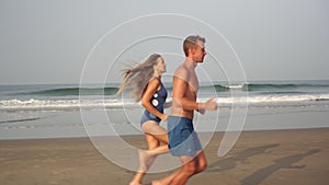Young couple man and woman run barefoot along the sandy beach against the background of the sea