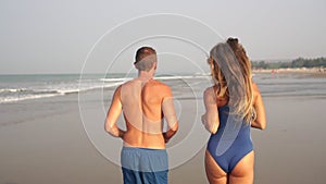 A young couple, a man and a woman, are running along the sea beach, slow motion