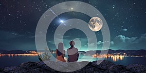 young couple man and woman sit on rock at night sea watching starry sky and big moon on horizon mediterranean city