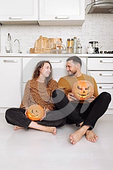 Young couple man and woman sitting on the floor at kitchen at home having fun and preparing for halloween talking laughing