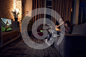 Young couple, man and woman spending time together at home in evening, sitting on couch and watching online football