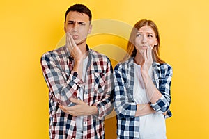 Young couple, man and woman suffering from toothache, holding on to the cheek, on yellow background