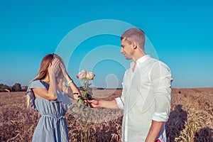 Young couple man woman, summer wheat field, happy smiling gives gift, bouquet of roses, surprise offer. Concept love