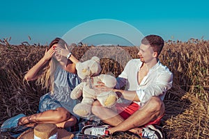 A young couple man woman, summer wheat field, happy smiling gives a gift, toy bear, rest. Concept of love, date, emotion