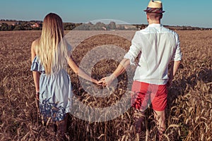 A young couple man woman, summer in wheat field, hold hands, walk and rest. Concept of love, date, emotion, tenderness