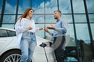 Young couple man and woman traveling together by new car having stop at charging station.