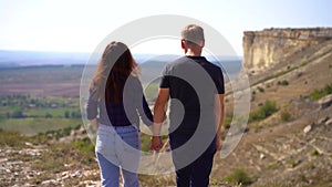Young couple man and woman walk forward with their backs to the camera view of the valley and mountains, slow motion