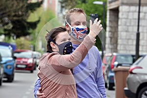Young couple, man and woman, wearing DIY facemasks, designed as EU and UK flag, taking a selfie