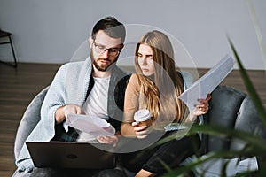 Young couple manages finances with laptop, looking through their bank accounts in the living room on the sofa